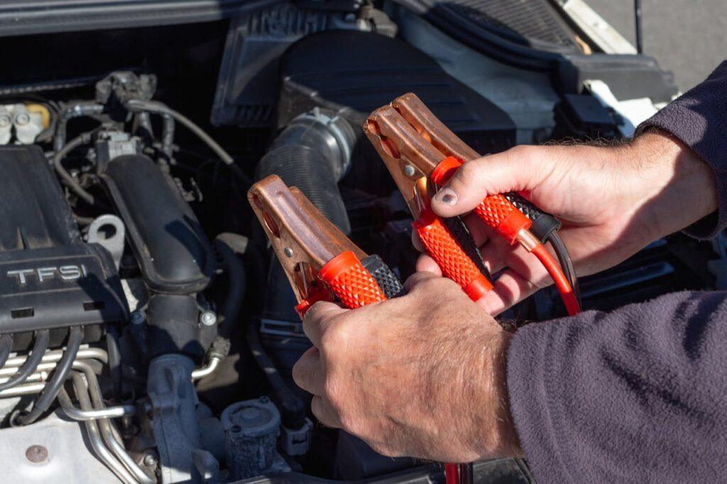 Close-up of hands holding jumper cables near a car engine, ready for repair.